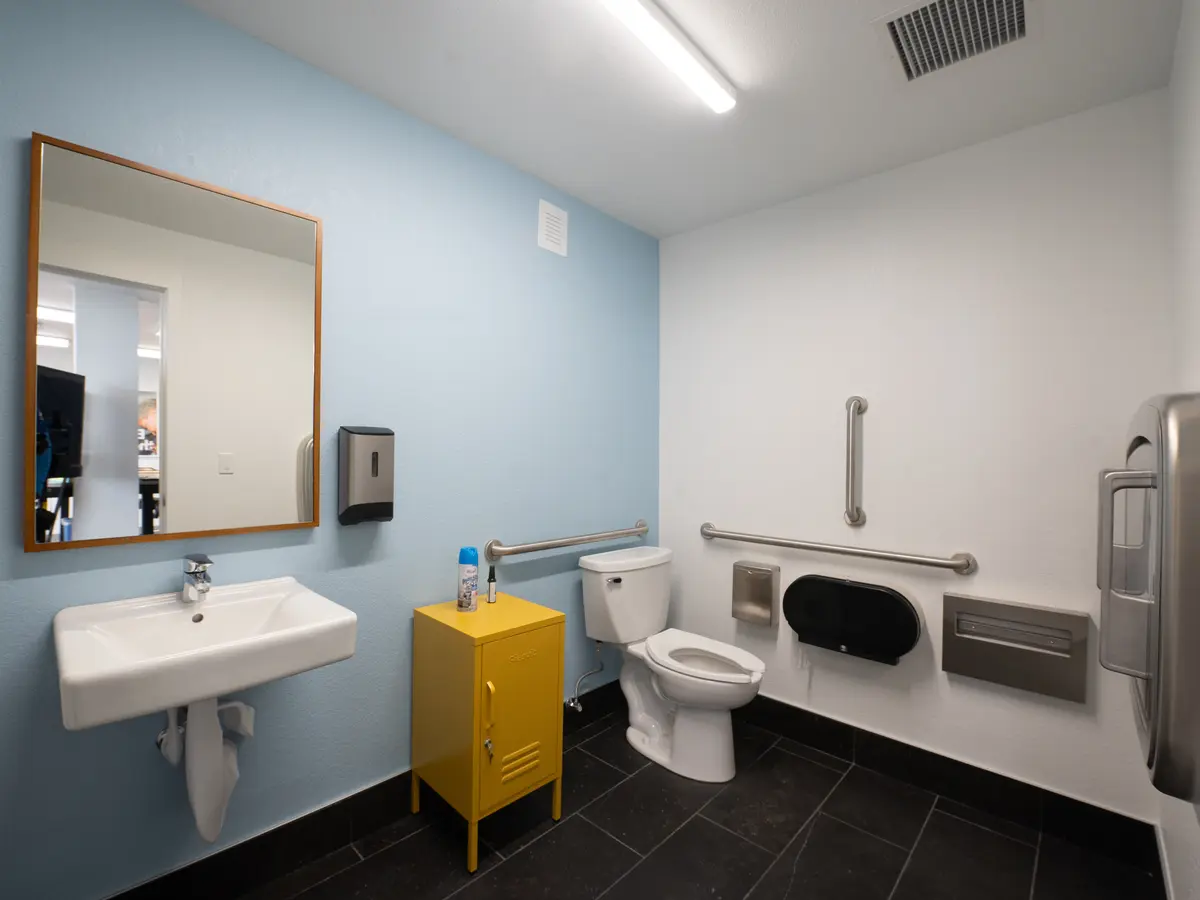 Completed accessible commercial restroom with grab bars, a wall-hung sink and tiled floor